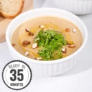 A white bowls of creamy vegan cauliflower soup, topped with olive oil, sliced almonds and cilantro with a time stamp in the bottom left hand corner | Hurry The Food Up