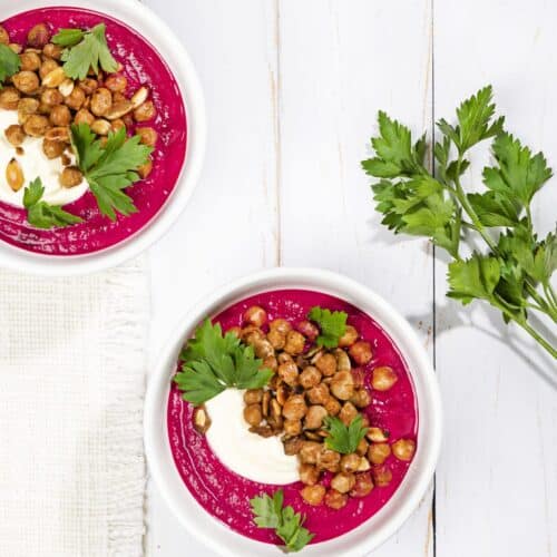 Birds eye view of two bowls of beetroot soup, with a decorative sprig of parsley next to them. | Hurry The Food Up