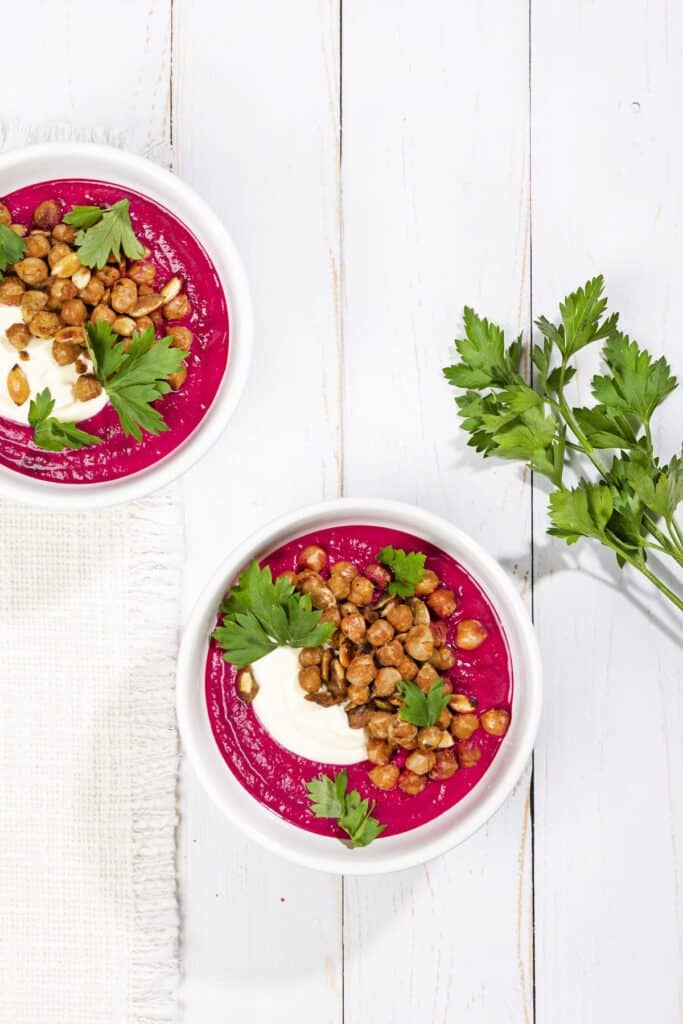 Birds eye view of two bowls of beetroot soup, with a decorative sprig of parsley next to them. | Hurry The Food Up