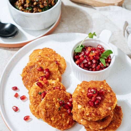 Roasted cottage cheese fritters are served on the white plate with a small dipping bowl of pomegranate salsa near them. Next to it there is a lentil chard side is in the small white bowl | Hurry The Food Up