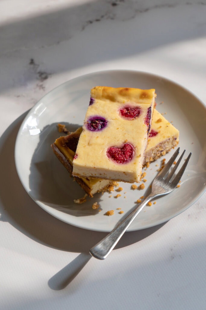 There is a white plate with two pieces of cottage cheesecake and a fork on the marble surface | Hurry The Food Up