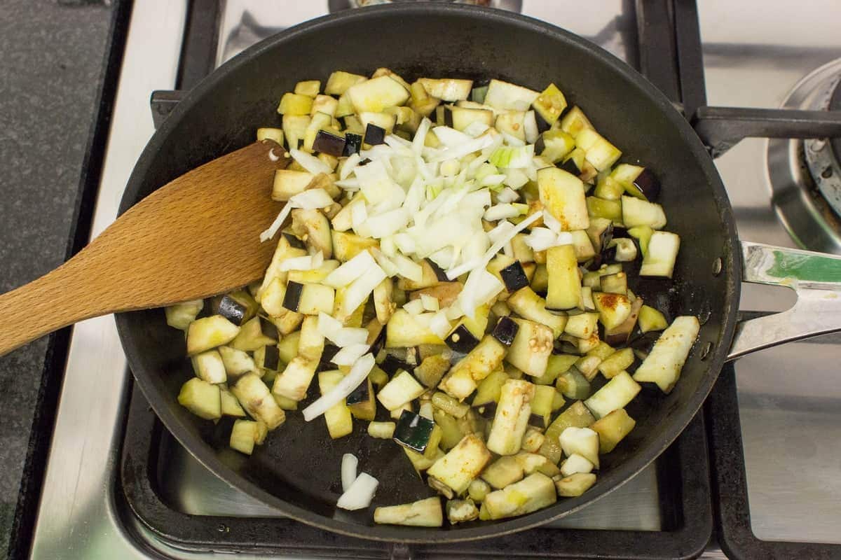 Aubergines and onion in a frying pan with a wooden spatula for stirring them, being fried up for sauce | Hurry The Food Up