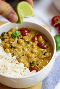 A bowl with Vegan Chickpea Curry. Someone drips lime juice for the Curry | HurryTheFoodUp